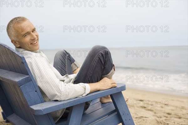 Portrait of mature man sitting in chair on beach