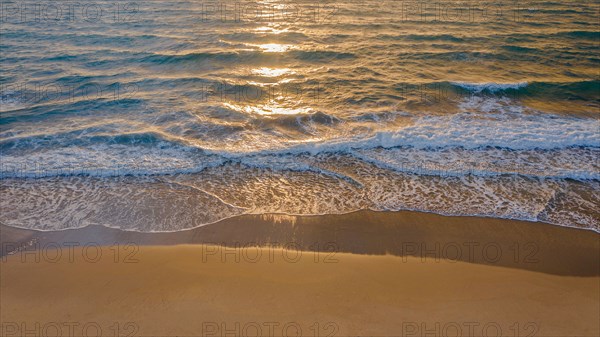 Calm ocean waves rolling onto sandy beach at sunrise