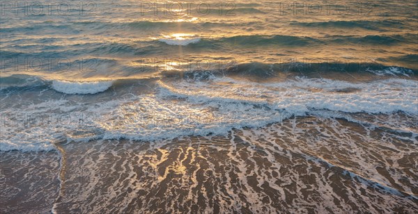 Calm ocean waves rolling onto sandy beach at sunrise