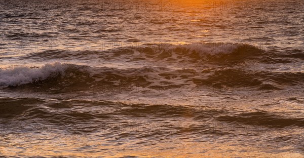 Close-up of ocean waves washing beach at sunrise