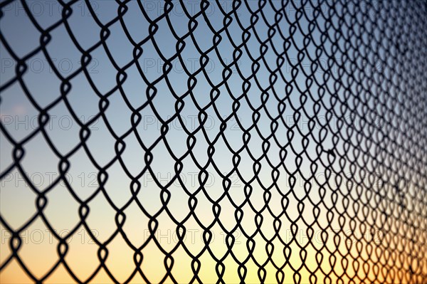 Chain link fence against sky at sunset