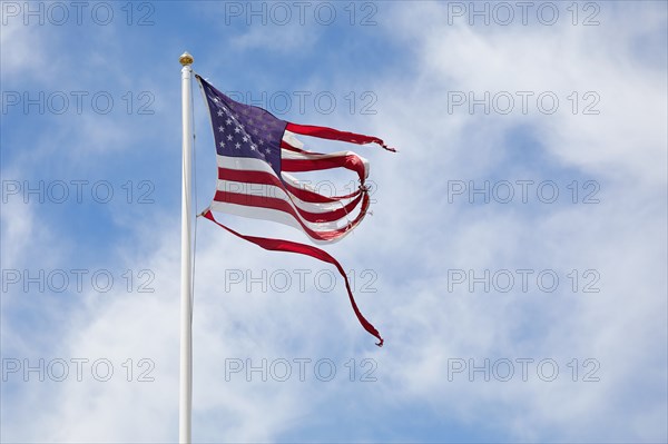 Torn American flag against sky