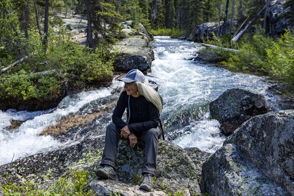 Senior blonde woman hiking by rushing stream in mountains near Sun Valley