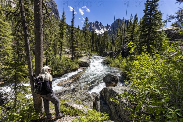 Senior blonde woman hiking by rushing stream in mountains near Sun Valley