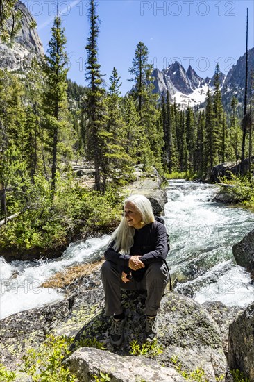 Senior blonde woman hiking by rushing stream in mountains near Sun Valley