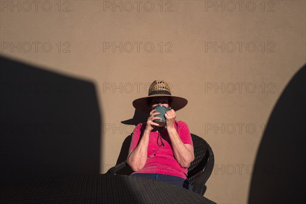 Woman drinking coffee against adobe wall on sunlit patio