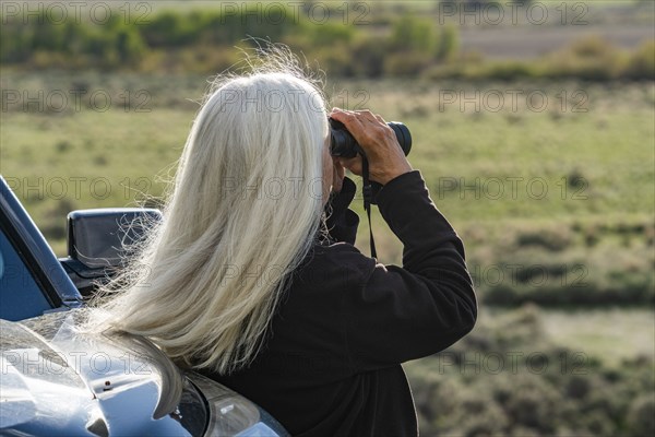 Rear view of woman looking through binoculars at car