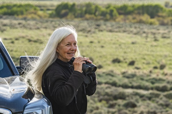 Smiling woman with binoculars at car in field