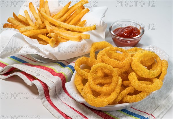 Fried onion rings and French fries with ketchup on tablecloth