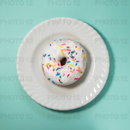 Overhead view of donut with white icing and sprinkles on white plate