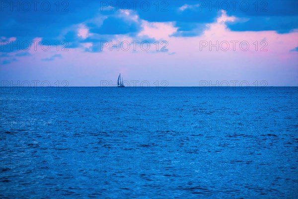 Ocean at sunrise with lone sailboat in distance