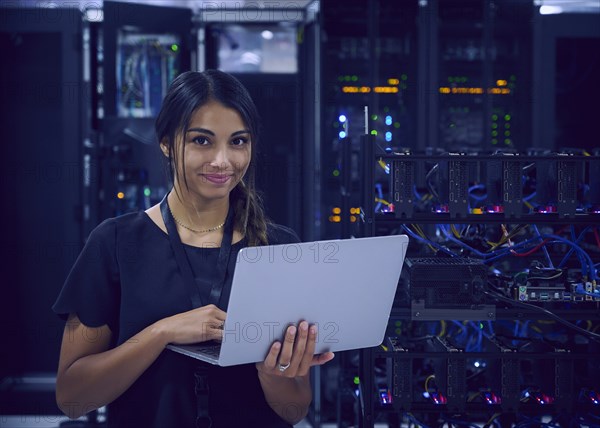 Portrait of smiling female technician with laptop in server room
