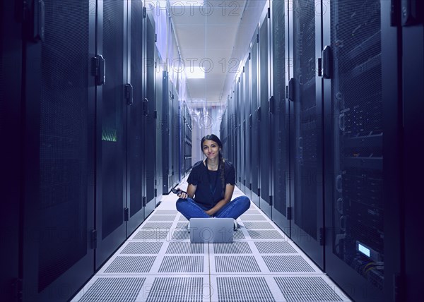 Portrait of female technician sitting on floor in server room