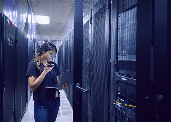 Female technician using smart phone and laptop in server room