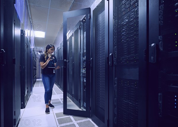 Female technician using smart phone and laptop in server room