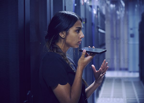 Female technician using smart phone in server room