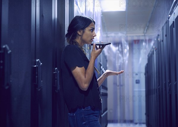 Female technician using smart phone in server room