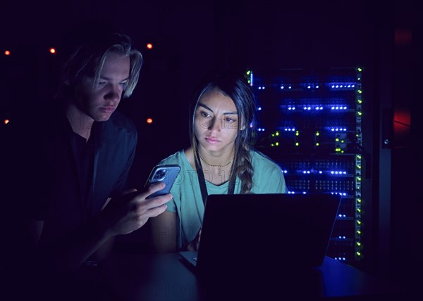 Technicians using laptop and smart phone in server room