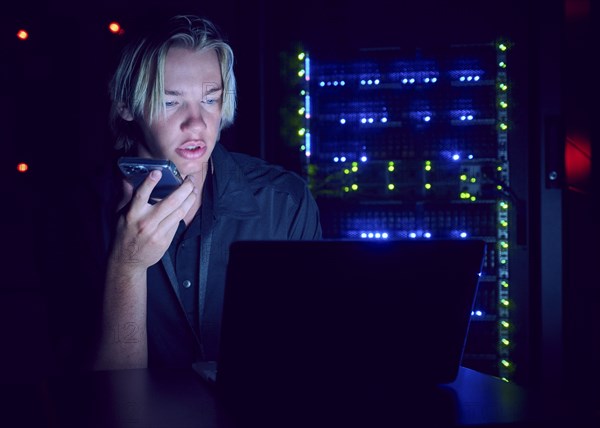 Technician using laptop and smart phone in server room