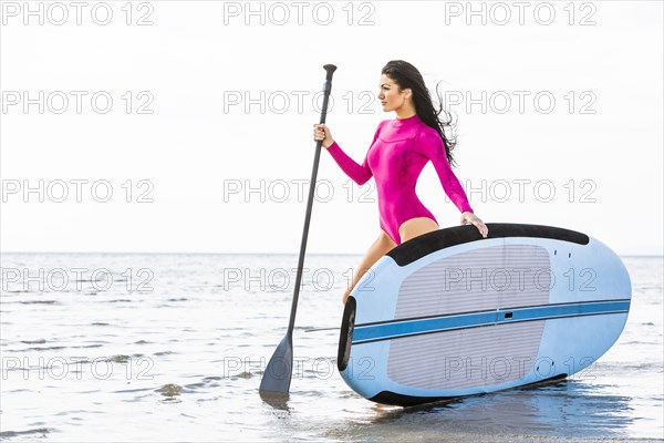 Woman in pink swimsuit standing with paddleboard by lake