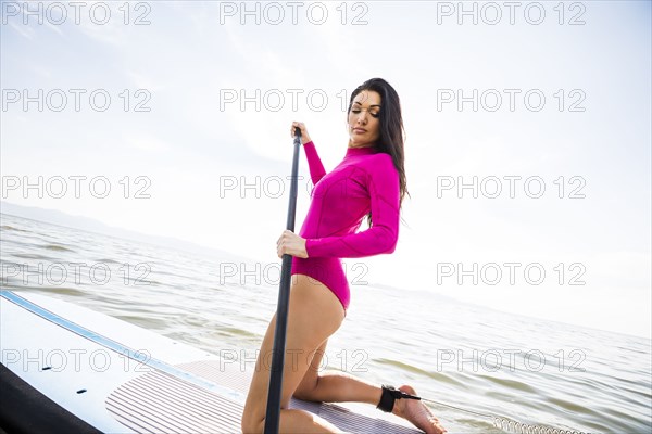 Woman in pink swimsuit kneeling on paddleboard on lake