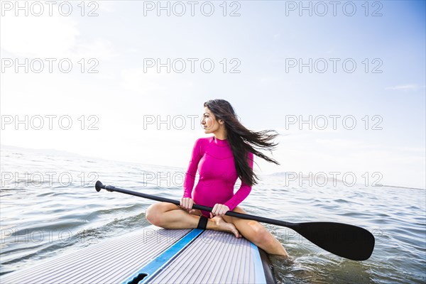 Woman in pink swimsuit sitting on paddleboard on lake