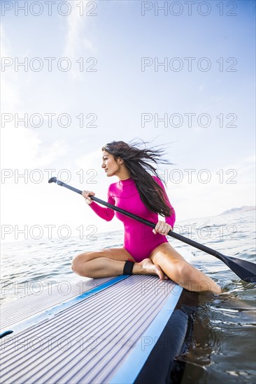 Woman in pink swimsuit sitting on paddleboard on lake