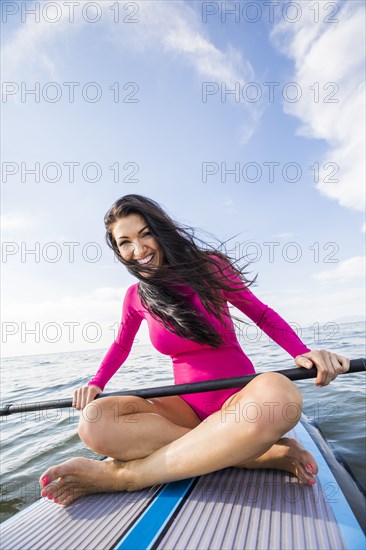 Portrait of smiling woman in pink swimsuit sitting on paddleboard on lake