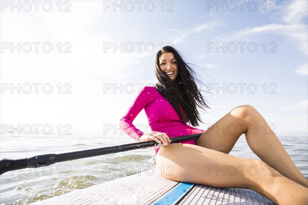 Portrait of smiling woman in pink swimsuit sitting on paddleboard on lake