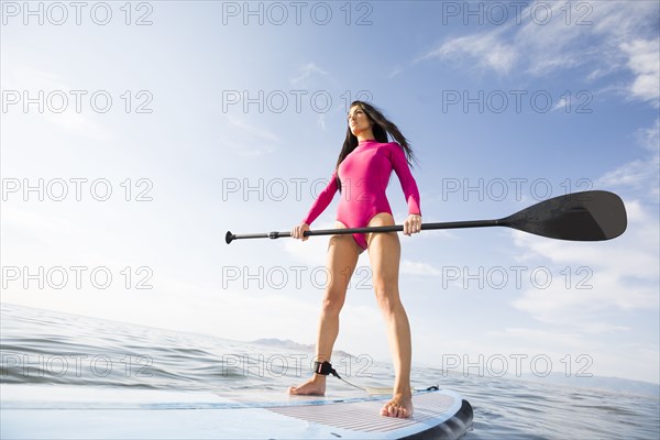 Woman in pink swimsuit standing on paddleboard on lake