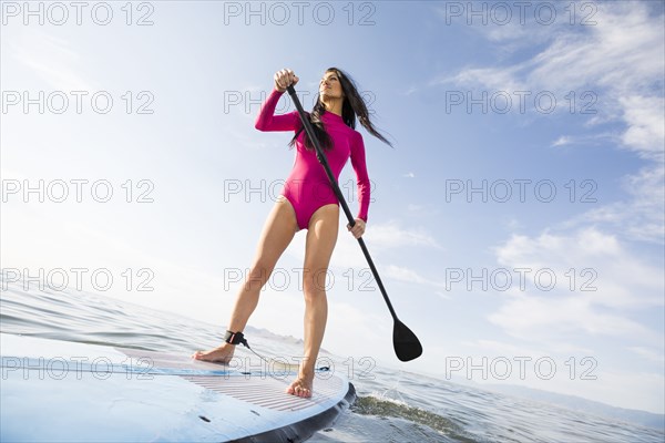 Woman in pink swimsuit paddleboarding on lake