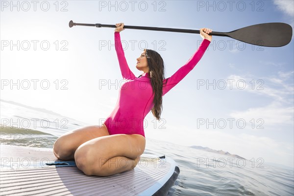 Woman in pink swimsuit kneeling on paddleboard on lake