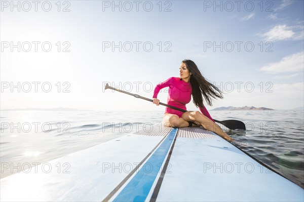 Woman in pink swimsuit sitting on paddleboard on lake