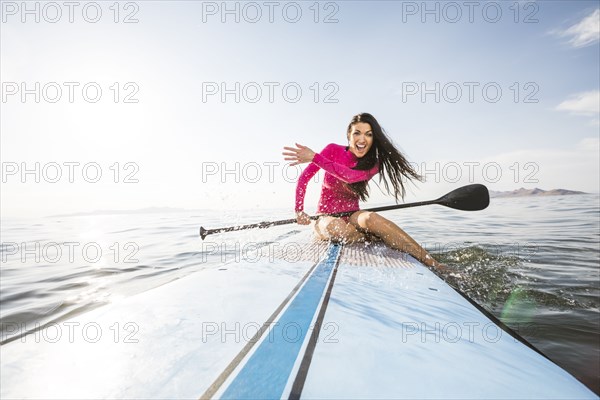 Smiling woman in pink swimsuit sitting on paddleboard and splashing water