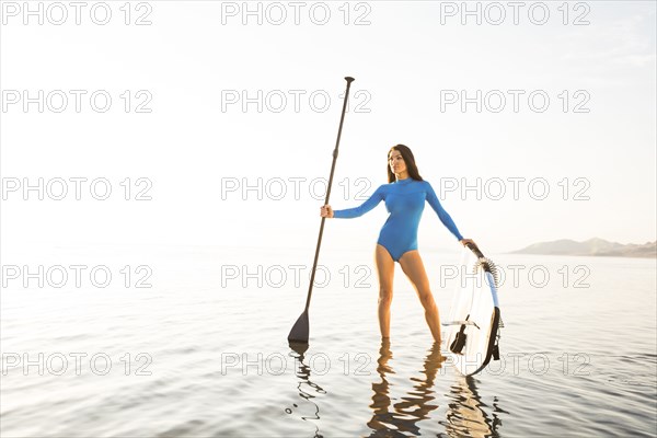 Portrait of woman in blue swimsuit with paddleboard in lake at sunset