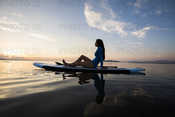 Woman in sitting on paddleboard on lake at sunset