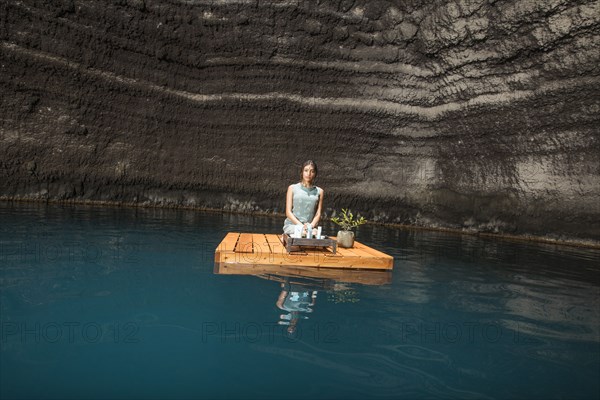 Beautiful woman kneeling on wooden raft on pond