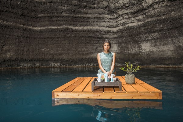 Beautiful woman kneeling on wooden raft on pond