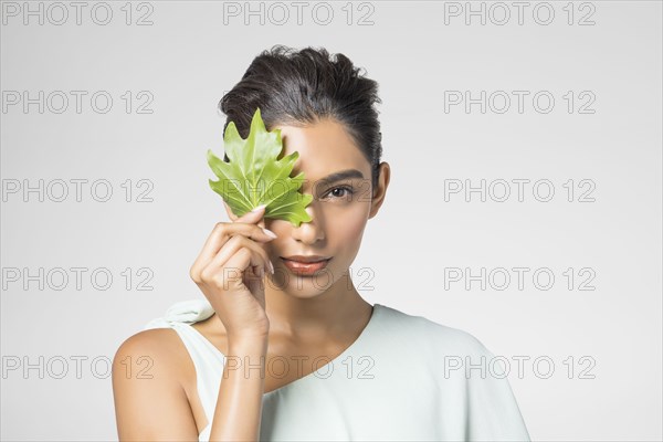Studio portrait of beautiful woman with leaf on her face