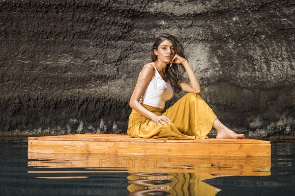 Beautiful woman sitting on wooden raft on pond