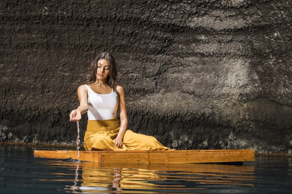 Beautiful woman sitting on wooden raft on pond