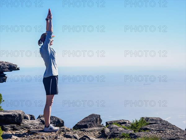 Woman standing on cliff with arms raised