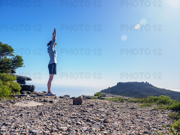 Woman standing on cliff with arms raised