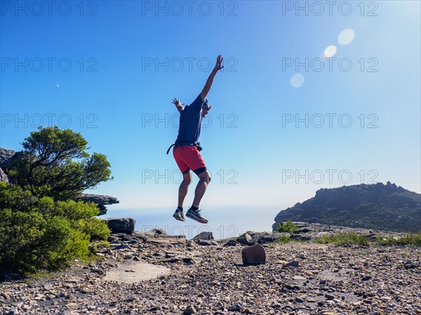 Man jumping on cliff with arms raised