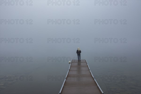 Back view of senior woman standing on jetty in morning