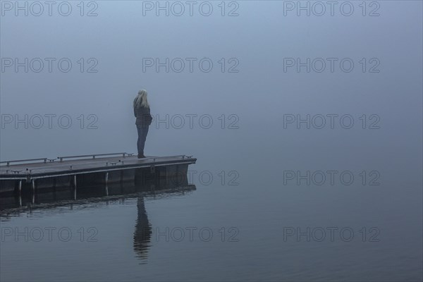 Senior woman standing on jetty in foggy morning