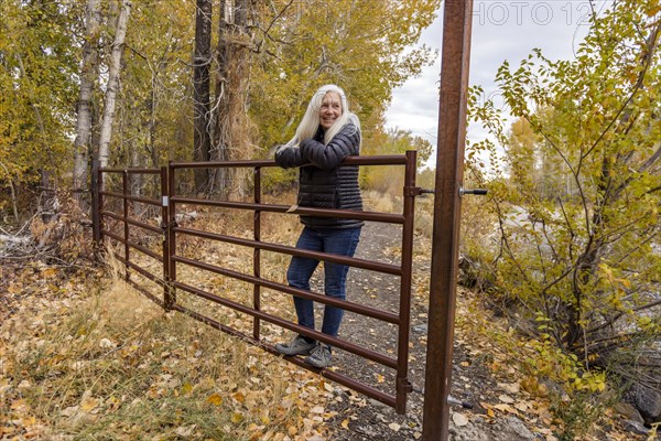 Senior blonde woman leaning on ranch gate