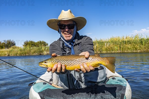 Senior fly fisherman holds brown trout before releasing back into spring creek