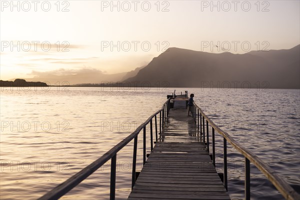 Boy standing on pier at lagoon at sunset