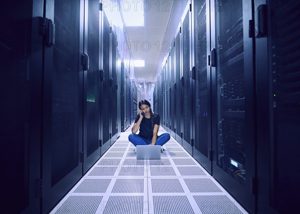 Female technician using laptop and phone in server room